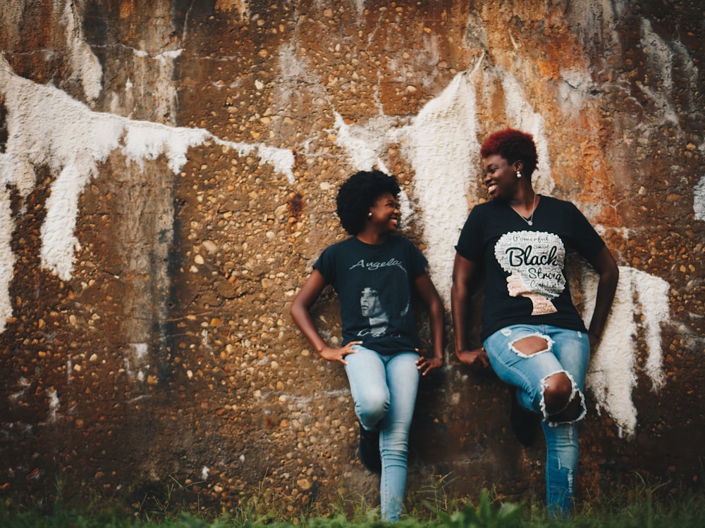 two women standing behind brown wall