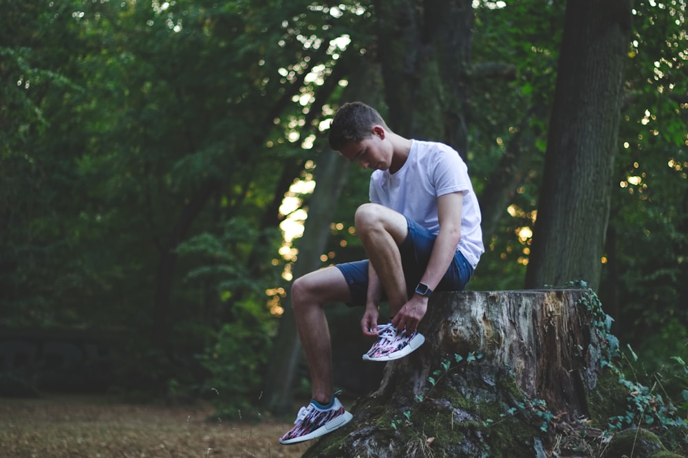 man sitting while holding shoe near trees