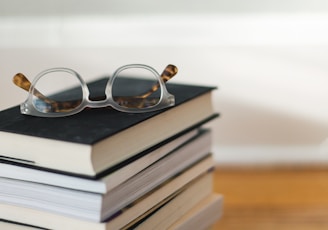 clear framed eyeglasses on top of pile of books