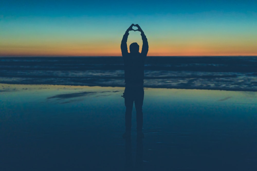 silhouette of person making heart sign near seashore