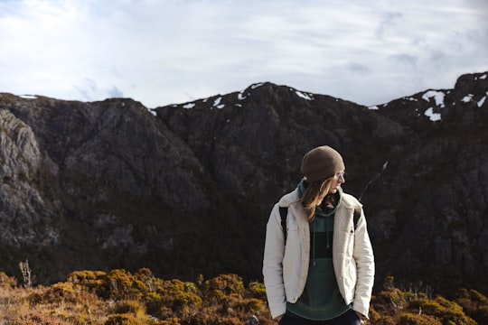 man wearing white jacket on cliff under white sky during daytime in Cradle Mountain Australia