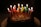 A chocolate cake topped with lit candles spelling out 'happy birthday'. The candles are colorful, and the backdrop is dark, making the flames stand out brightly against the cake.