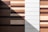 A vertical composition of alternating wood and white panels creates a geometric pattern. The wood panels vary in shades of brown, from light to dark, and are horizontally aligned. A sharp triangular shadow cuts diagonally across the center of the image, adding contrast and depth to the pattern.