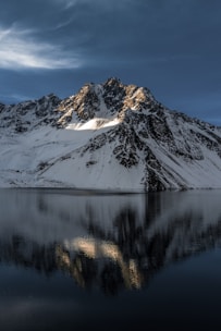 A cinematic 4k image of a snow-capped mountain peak mirrored perfectly in a dark, still lake under a twilight sky.