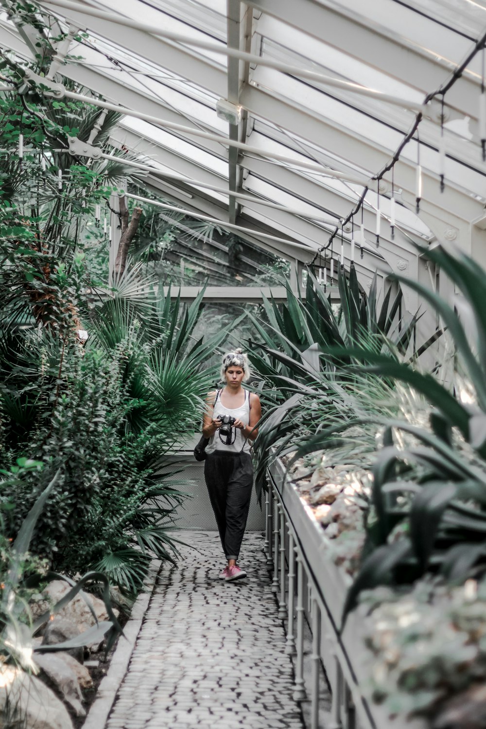 woman walking on pathway beside plants inside greenhouse