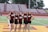 A group of five cheerleaders stand in a row on a sports field. They are wearing matching maroon tops with the letters LBMS and black skirts. The background consists of empty bleachers and trees.