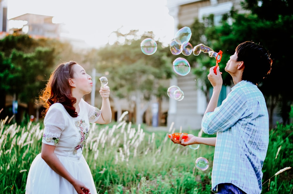 girl and man blowing bubbles near grass at daytime