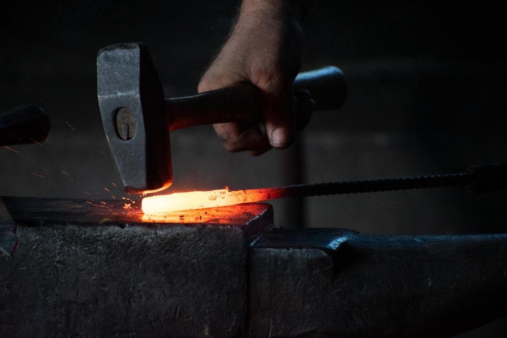 man pounding hammer on hot iron rod