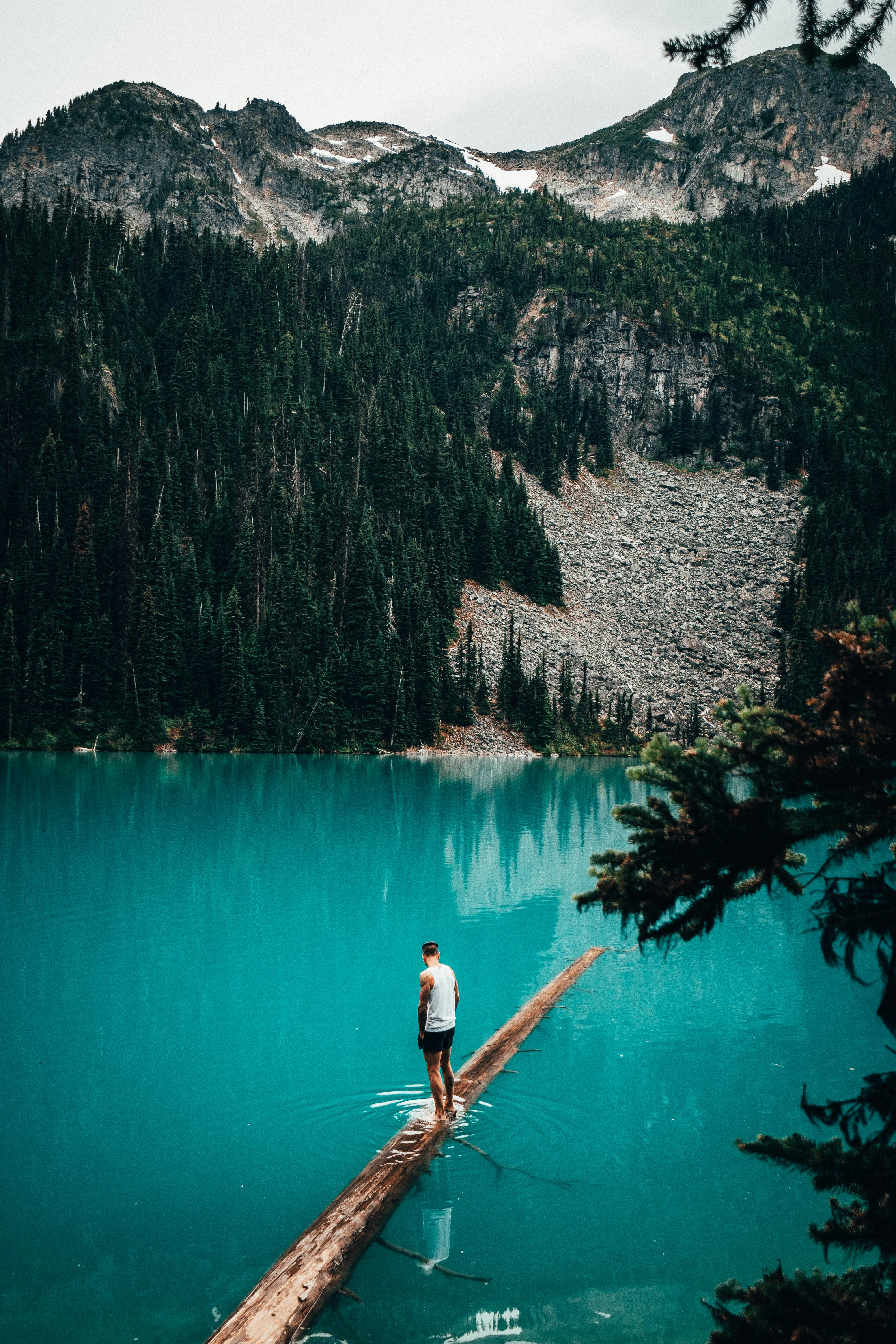 man standing on brown log on body of water