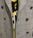 A close-up view of a plaid-patterned blazer featuring metallic buttons and layered over a yellow and black patterned fabric.