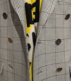 A close-up view of a plaid-patterned blazer featuring metallic buttons and layered over a yellow and black patterned fabric.