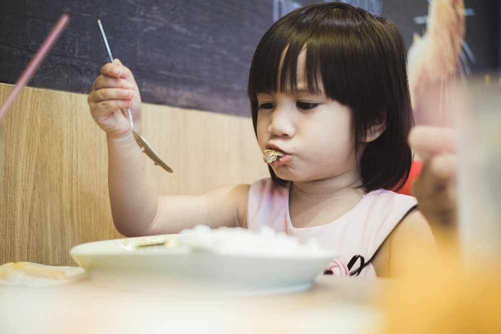 Mädchen isst, während sie einen Löffel über dem Teller hält
