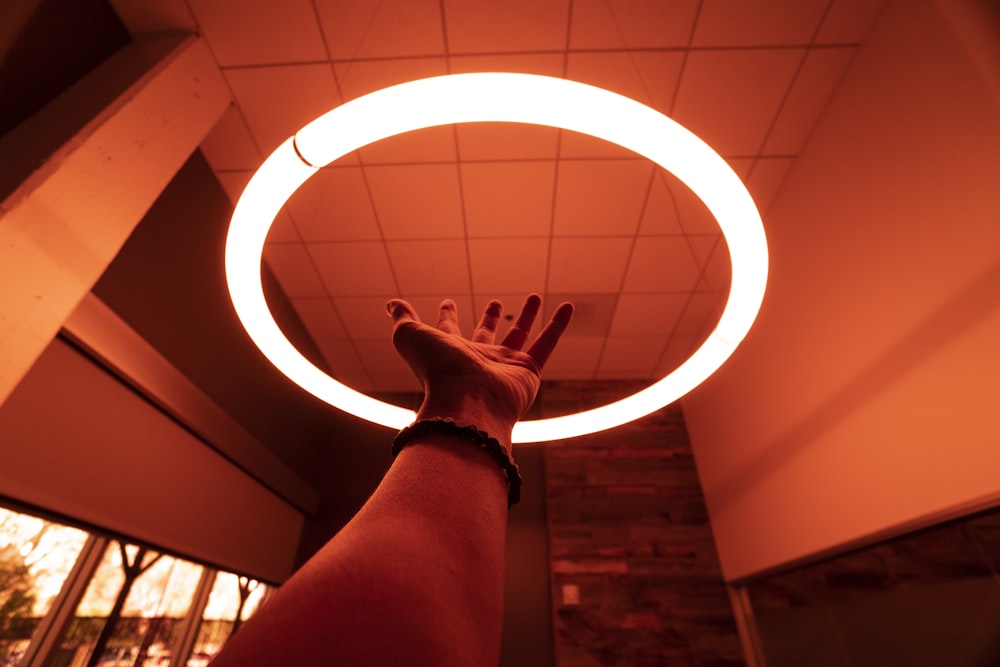 person reaching round turned-on fluorescent lamp in room