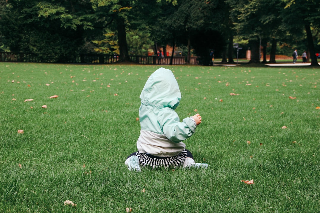 toddler sitting on green grass at daytime