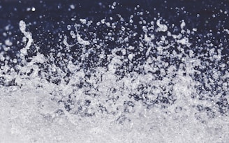A dynamic spray of water droplets suspended in the air against a dark background, capturing the motion and energy of splashing water.