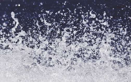 A dynamic spray of water droplets suspended in the air against a dark background, capturing the motion and energy of splashing water.