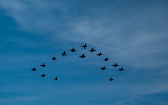A formation of fighter jets flying in a V-shape against a backdrop of a clear blue sky.