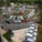 A circular parking lot is filled with a variety of cars arranged neatly in rows. Trees and small shrubs decorate the central area, adding greenery amidst the vehicles. A few traffic cones are visible, guiding the flow of cars. The scene is captured from an elevated viewpoint, providing a comprehensive view of the bustling parking area.