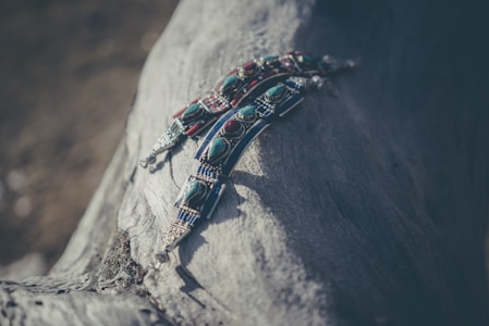 Intricately detailed beaded jewelry with turquoise and red stones laid on a textured piece of driftwood. The materials have a handcrafted, rustic feel, and the image is softly lit creating a tranquil and artistic atmosphere.