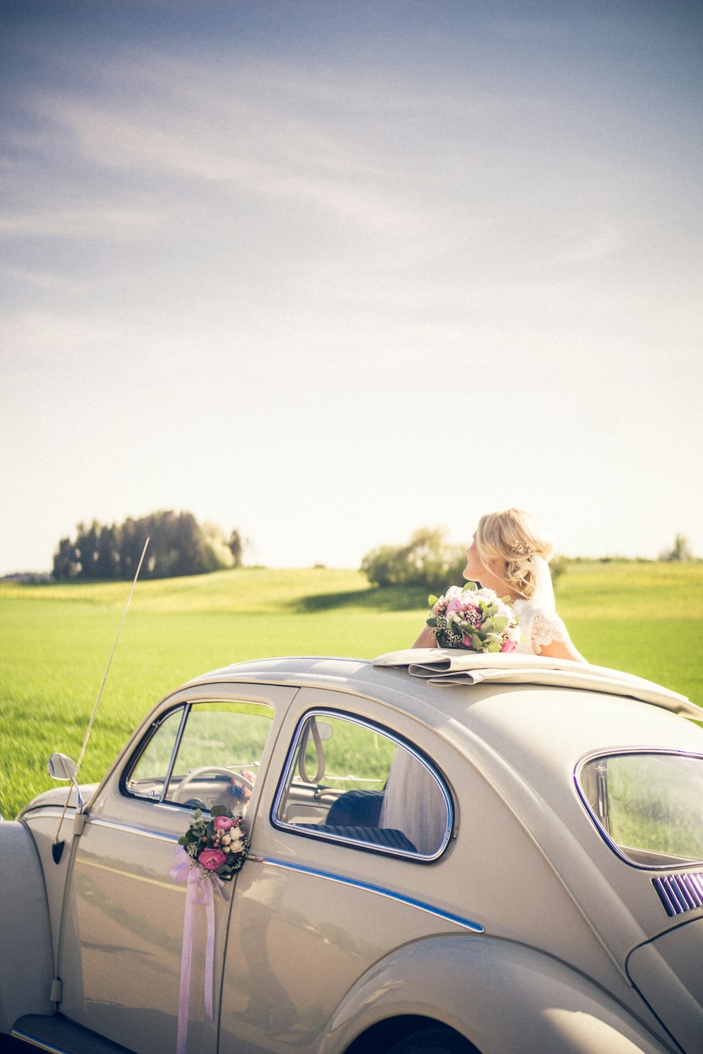 woman wearing wedding dress standing inside the white Volkswagen Beetle