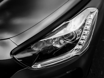 A close-up view of a sleek, modern car headlight featuring an intricate design with clear glass and LED lights, set against a smooth metallic body.