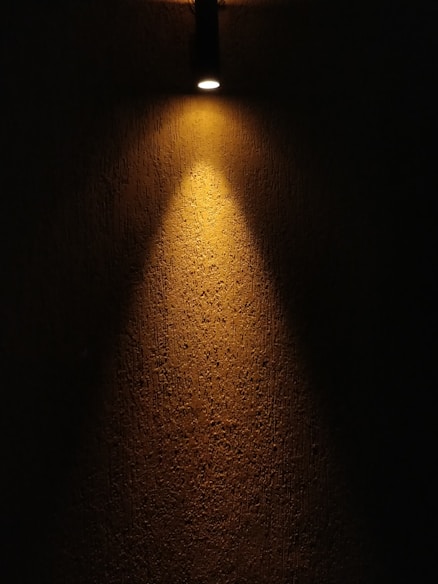 Close-up of a golden spotlight casting warm light on a textured wall.