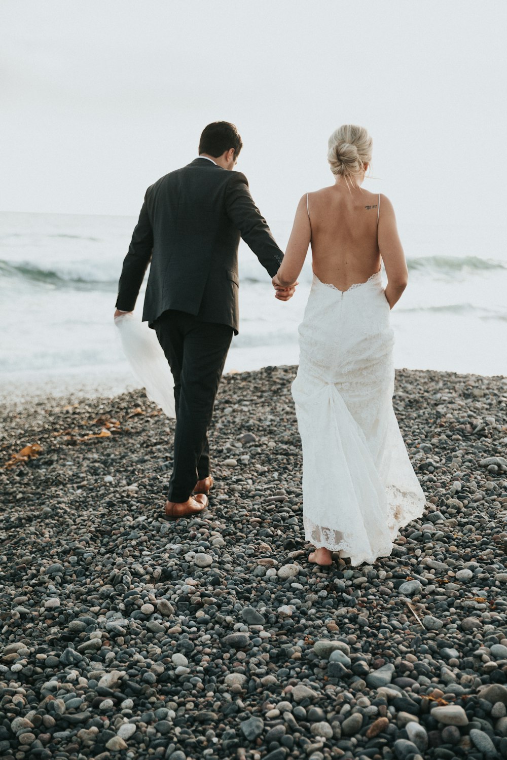 Noivo e noiva caminhando em pedra perto do corpo de água