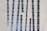 Tall narrow windows with blue-tinted glass are set vertically in an abstract pattern on a modern concrete building facade. The windows are of varying heights and are placed at slight angles, creating a dynamic visual effect.