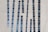 Tall narrow windows with blue-tinted glass are set vertically in an abstract pattern on a modern concrete building facade. The windows are of varying heights and are placed at slight angles, creating a dynamic visual effect.