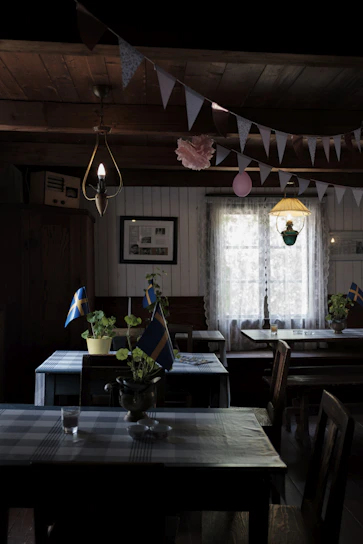 Warm Scandinavian-style dining area softly lit, with rustic wooden tables and plush velvet cushions in deep crimson and forest green.