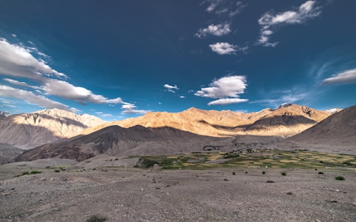 A sunlit desert homestead with solar panels and a thriving garden surrounded by rugged mountain terrain.