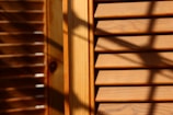 Wooden window blinds with horizontal slats are visible, with shadows cast across the surface. The lighting creates a warm and textured appearance, highlighting the natural grain of the wood.