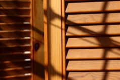 Wooden window blinds with horizontal slats are visible, with shadows cast across the surface. The lighting creates a warm and textured appearance, highlighting the natural grain of the wood.