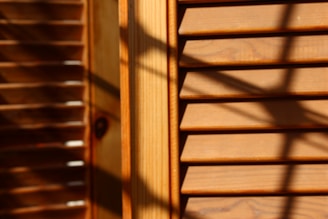 Wooden window blinds with horizontal slats are visible, with shadows cast across the surface. The lighting creates a warm and textured appearance, highlighting the natural grain of the wood.