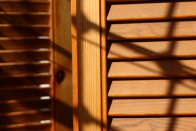 Wooden window blinds with horizontal slats are visible, with shadows cast across the surface. The lighting creates a warm and textured appearance, highlighting the natural grain of the wood.
