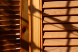 Wooden window blinds with horizontal slats are visible, with shadows cast across the surface. The lighting creates a warm and textured appearance, highlighting the natural grain of the wood.