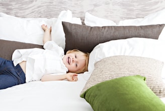 A cheerful child tucked into soft, colorful bedding with playful patterns in a bright, cozy bedroom.
