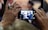 A close-up shot of hands holding a smartphone displaying a photograph of a group of people. The image on the phone shows individuals dressed in formal attire indoors, possibly at an event or gathering. The focus on the phone suggests capturing a moment of significance.