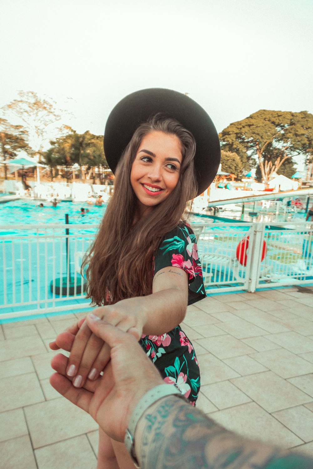 Frau steht und lächelt, während sie Händchen einer anderen Person in der Nähe des Schwimmbades hält