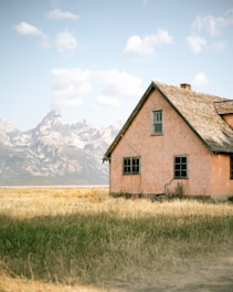 A newly built rustic-style home framed by towering rocky mountains under a clear blue sky.
