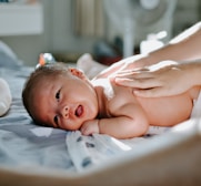 baby laying on bed while woman massaging his back