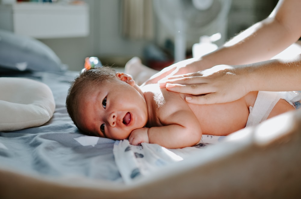 bébé allongé sur le lit pendant qu’une femme lui masse le dos