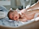 baby laying on bed while woman massaging his back