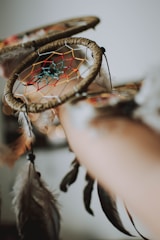 A dreamcatcher with a detailed woven pattern adorned with colorful threads is prominently featured. It has a circular shape with a web-like structure in the center, decorated with feathers hanging from it.