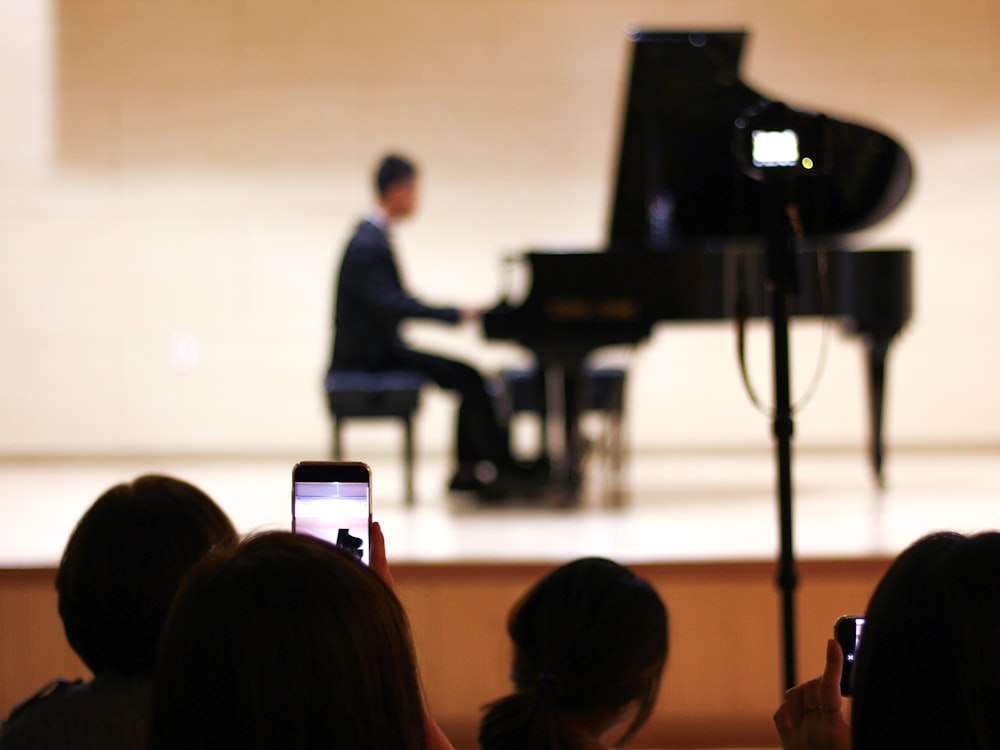 person taking photo of person playing piano on stage