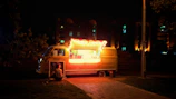 Street food truck Mamabowl in action with neon red and yellow lights glowing at dusk.