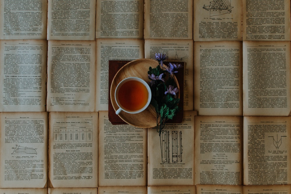 cup of coffee beside purple flowers on top of book