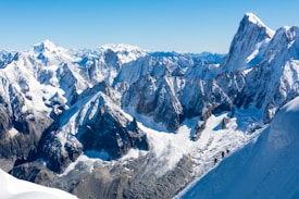 A stunning view of snow-capped mountain peaks under a clear blue sky. Several climbers can be seen ascending one of the slopes, adding a sense of scale to the vast landscape.