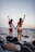 two women standing on rock while raising their hands near sea during daytime