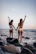 two women standing on rock while raising their hands near sea during daytime